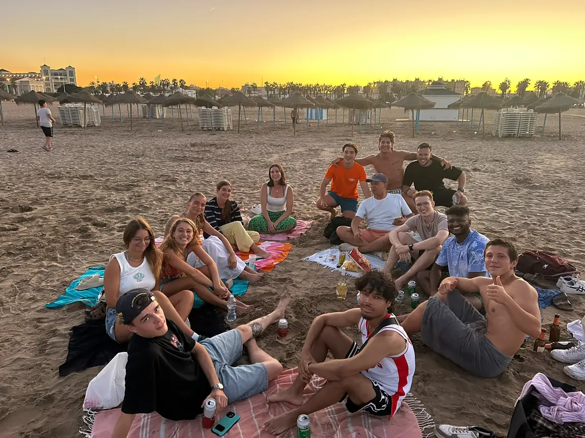 Miembros de la comunidad Nexo sentados juntos en la playa de la Malvarrosa de Valencia al atardecer